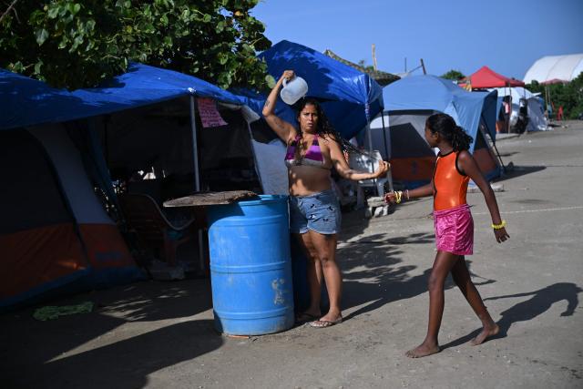A woman displaced following twin earthquakes that struck the region bathes with water from a tank at 'Ciudad Carpita', an improvised shelter in Mare Abajo, La Guaira state, Venezuela, on July 14, 2026, . The death toll from the deadly earthquakes that hit Venezuela on June 14 has surpassed 4,700, while almost 17,000 people have been injured, an official report released on July 14 stated. (Photo by Raul ARBOLEDA / AFP)