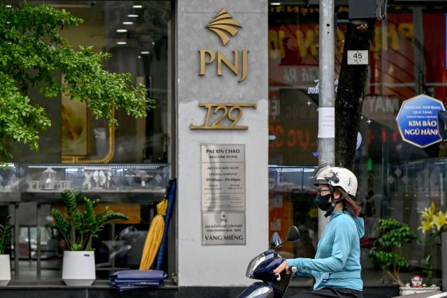 A woman rides a motorbike past a Phu Nhuan Jewelry (PNJ) store in Hanoi on July 15, 2026. Police in Vietnam are investigating an international diamond ring accused of smuggling in 28,000 diamonds worth nearly $11 million, with the country's largest jeweller Phu Nhuan Jewelry (PNJ) caught up in the probe. (Photo by Nhac NGUYEN / AFP)