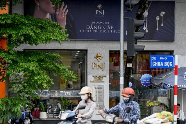 People ride motorbikes past a Phu Nhuan Jewelry (PNJ) store in Hanoi on July 15, 2026. Police in Vietnam are investigating an international diamond ring accused of smuggling in 28,000 diamonds worth nearly $11 million, with the country's largest jeweller Phu Nhuan Jewelry (PNJ) caught up in the probe. (Photo by Nhac NGUYEN / AFP)