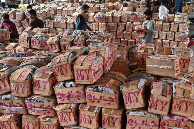Labourers walk past mango crates at a wholesale market in Lahore on July 15, 2026. (Photo by Arif ALI / AFP)
