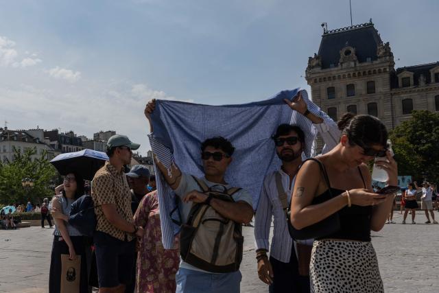Visitors attempt to shade from the sun with a scarf as they queue to enter the Notre-Dame Cathedral (unseen) amid a heatwave in central Paris on July 14, 2026. The Paris region, and large parts of the rest of France, is currently experiencing the third heatwave since May 2026, increasing the risk of fires. The three heatwaves have seen temperature records broken in several countries across Europe and have caused thousands of excess deaths, according to estimates in Belgium, Britain, France and Spain. (Photo by Martin LELIEVRE / AFP)