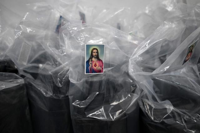 This image shows packs of rolls of body bags bearing the Sacred Heart of Jesus prayer cards for the earthquakes victims, at the ByEfrainMogollon workshop in Maracay, state of Aragua, Venezuela, on July 13, 2026. At a fashion workshop in Venezuela, the sewing machines set aside the brightly coloured threads used to make elegant dresses to sew body bags, which the creative director decided to donate to rescue workers, volunteers and relatives recovering bodies from the buildings that collapsed following the twin earthquakes measuring 7.2 and 7.5. (Photo by Raul ARBOLEDA / AFP)