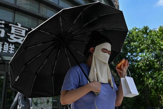 A woman protects herself from the sun with a umbrella and a face mask while walking on a street in Shanghai on July 15, 2026. (Photo by Hector RETAMAL / AFP)