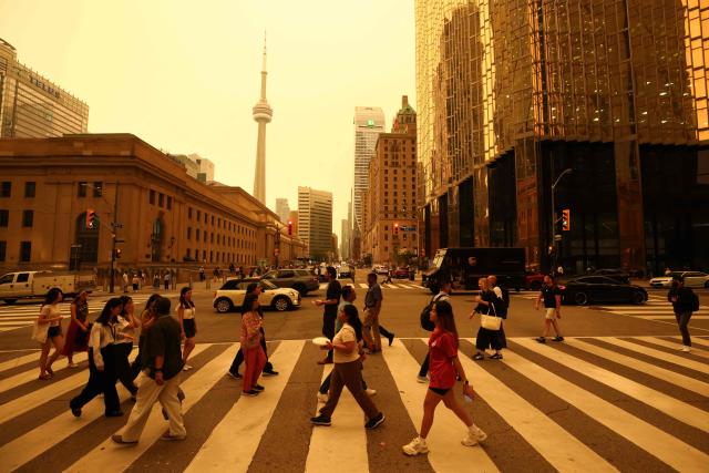 People walk in downtown Toronto, as smoke from forest fires in Northern Ontario causes poor air quality over the city, in Toronto, Ontario, Canada, July 15, 2026. (Photo by Cole BURSTON / AFP)