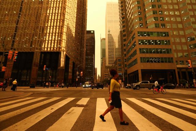 People walk in downtown Toronto, as smoke from forest fires in Northern Ontario causes poor air quality over the city, in Toronto, Ontario, Canada, July 15, 2026. (Photo by Cole BURSTON / AFP)