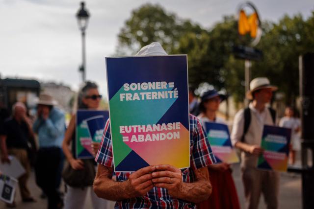 A protester holds a sign against euthanasia and assisted dying during a protest near the French National Assembly in Paris on July 15, 2026. French lawmakers on July 15, 2026, adopted a bill to establish a right to assisted dying for some adults suffering from an incurable condition. (Photo by Dimitar DILKOFF / AFP)