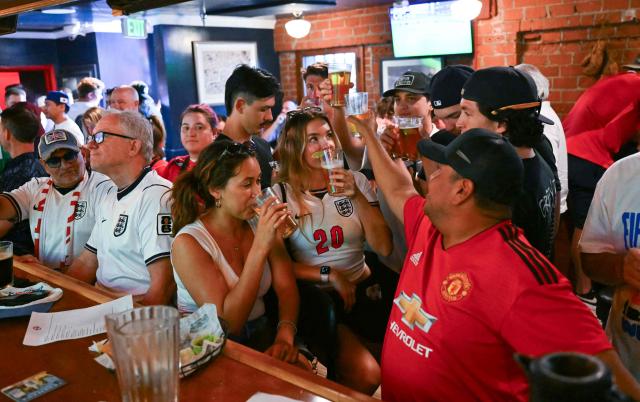 England fans cheer while holding glasses of beer as they watch the 2026 World Cup semi-final match between England and Argentina at the Underground Pub & Grill in Hermosa Beach, California, on July 15, 2026. (Photo by Patrick T. Fallon / AFP)