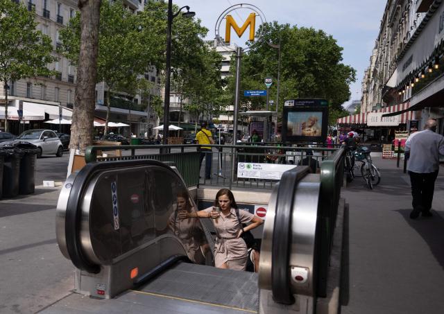 A commuter uses a smartphone as she exits a metro station riding an escalator in central Paris on July 15, 2026. (Photo by Martin LELIEVRE / AFP)