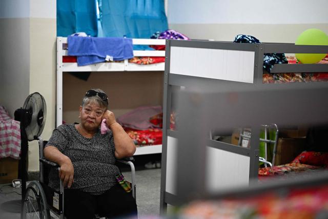 An earthquake-displaced resident from La Guaira sits in a wheelchair next to bunk beds inside a temporary shelter at the Jose Gervasio Artigas Educational Complex in Propatria, Caracas, on July 15, 2026, following the June 24 twin earthquakes. The death toll from the earthquakes that struck Venezuela almost three weeks ago has surpassed 4,700, while almost 17,000 people have been injured, an official report released on July 14, 2026 stated. (Photo by Federico PARRA / AFP)
