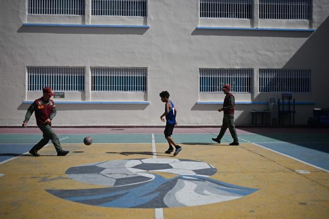 An earthquake-displaced child from La Guaira plays football with members of the National Guard inside a temporary shelter at the Jose Gervasio Artigas Educational Complex in Propatria, Caracas, on July 15, 2026, following the June 24 twin earthquakes. The death toll from the earthquakes that struck Venezuela almost three weeks ago has surpassed 4,700, while almost 17,000 people have been injured, an official report released on July 14, 2026 stated. (Photo by Federico PARRA / AFP)