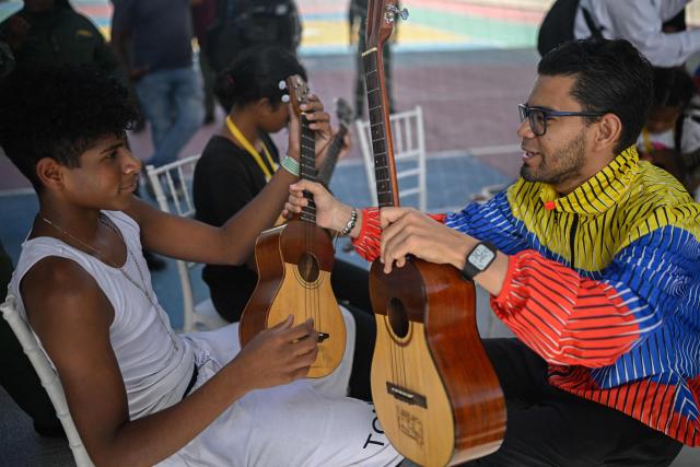 A volunteer from Venezuela's El Sistema music programme gives a cuatro lesson to displaced people from La Guaira at a temporary shelter at the Jose Gervasio Artigas Educational Complex in Propatria, Caracas, on July 15, 2026, following the June 24 twin earthquakes. The death toll from the earthquakes that struck Venezuela almost three weeks ago has surpassed 4,700, while almost 17,000 people have been injured, an official report released on July 14, 2026 stated. (Photo by Federico PARRA / AFP)