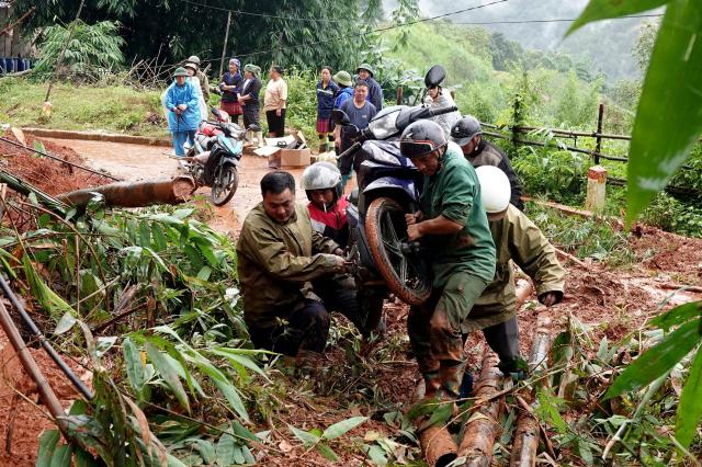People carry a motorbike across a landslide site in Mu Cang Chai Commune in Lao Cai Province, northern Vietnam on July 18, 2026. Severe flooding and landslides caused by heavy rains killed at least four people in Vietnam, state media reported. (Photo by A Lu / AFP)