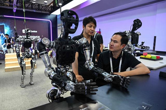 Workers are pictured with a humanoid robot by PND Botics during the World Artificial Intelligence Conference (WAIC) in Shanghai on July 18, 2026. (Photo by Hector RETAMAL / AFP)