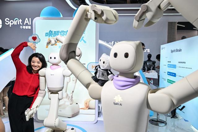 A woman poses next to humanoid robots by Spirit AI during the World Artificial Intelligence Conference (WAIC) in Shanghai on July 18, 2026. (Photo by Hector RETAMAL / AFP)