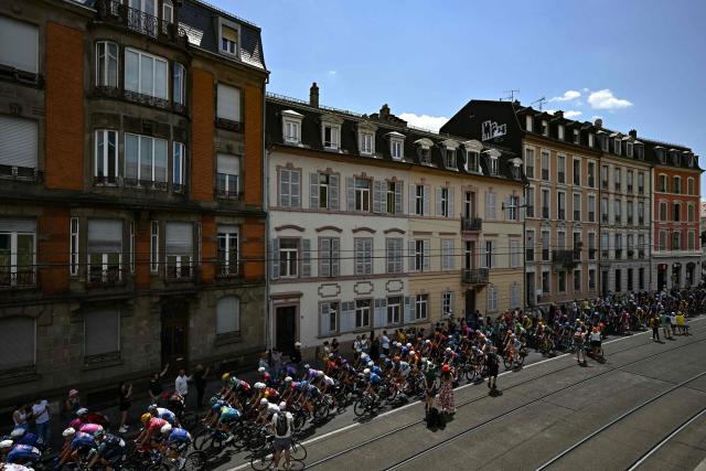 The pack of riders (peloton) cycles in the streets of Mulhouse at the start of the 14th stage of the 113th edition of the Tour de France cycling race, 155,3 km between Mulhouse and Le Markstein in the Vosges mountains, on July 18, 2026. (Photo by Loic VENANCE / AFP)