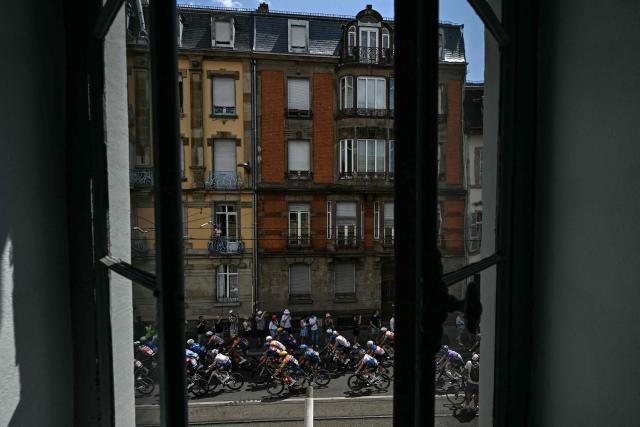 The pack of riders (peloton) cycles in the streets of Mulhouse at the start of the 14th stage of the 113th edition of the Tour de France cycling race, 155,3 km between Mulhouse and Le Markstein in the Vosges mountains, on July 18, 2026. (Photo by Loic VENANCE / AFP)