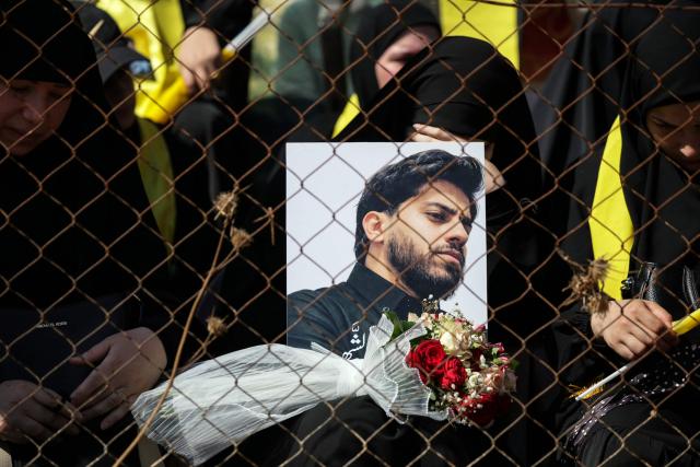 A woman holds a portrait of a Hezbollah fighter who was killed in clashes with the Israeli army during a mass funeral in the southern Lebanese village of Majdel Selm on July 18, 2026. Lebanese President Joseph Aoun on July 18 left Beirut for Washington, where he is expected to meet Donald Trump, the Lebanese presidency said, after talks between Lebanon and Israel wrapped up in Italy. Hezbollah pulled Lebanon into the Middle East war on March 2, when it began striking Israel in support of its backer Tehran. (Photo by Ibrahim AMRO / AFP) / 