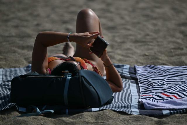 A beach goer looks at her phone at Le Racou beach in Argeles-sur-Mer, on the Mediterranean coast in southwestern France, on July 18, 2026. (Photo by Lionel BONAVENTURE / AFP)