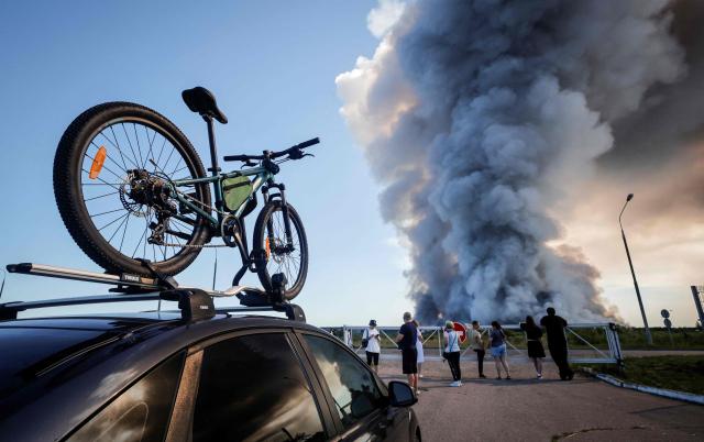 Bystanders watch as smoke rises from a fire at the Russian e-commerce firm Wildberries' logistics complexes in the town of Elektrostal outside Moscow on July 18, 2026. A Ukrainian drone attack on two logistics centres in Russia killed eight people and injured 24, officials said on July 18, 2026, when the Moscow region reported a new wave of drone strikes. Russian e-commerce firm Wildberries said its logistics complexes in Kotovsk and Elektrostal, in the Tambov and Moscow regions respectively, came under attack. One person was killed and 37 were injured at the Elektrostal warehouse, according to the region's governor, Andrei Vorobyov. (Photo by TATYANA MAKEYEVA / AFP)