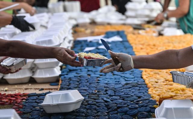 People serve portions of a giant cake in the colors of the Venezuelan national flag, to be distributed in the shelters to the people affected by the June 24 earthquakes, in Caracas on July 18, 2026. (Photo by Juan BARRETO / AFP)