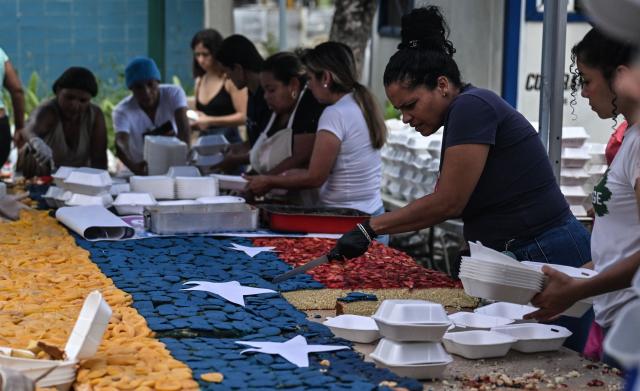People serve portions of a giant cake in the colors of the Venezuelan national flag, to be distributed in the shelters to the people affected by the June 24 earthquakes, in Caracas on July 18, 2026. (Photo by Juan BARRETO / AFP)