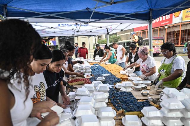 People pack portions of a giant cake in the colors of the Venezuelan national flag, to be distributed in the shelters to the people affected by the June 24 earthquakes, in Caracas on July 18, 2026. (Photo by Juan BARRETO / AFP)