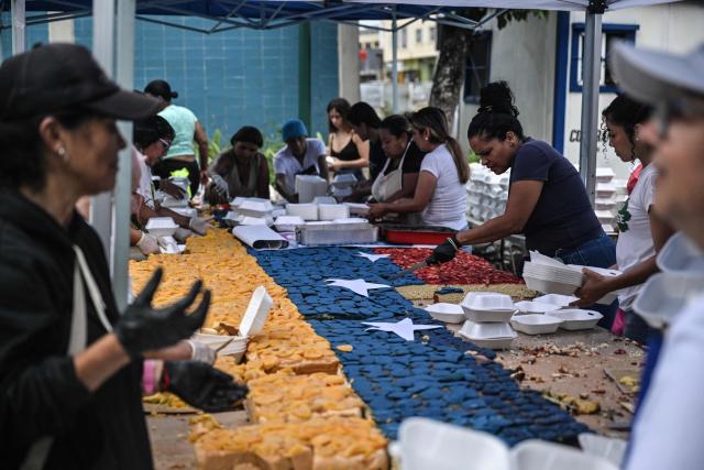 People serve portions of a giant cake in the colors of the Venezuelan national flag, to be distributed in the shelters to the people affected by the June 24 earthquakes, in Caracas on July 18, 2026. (Photo by Juan BARRETO / AFP)