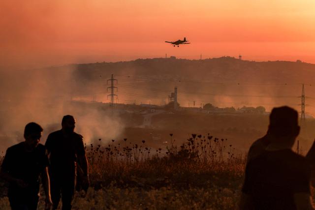 Palestinians watch as an Israeli firefighting plane extinguishes a blaze near the village of Tell, adjacent to the Israeli settlement of Havat Gilad, west of Nablus in the occupied West Bank on July 18, 2026, after a reported arson attack by Israeli settlers on the village, according to eyewitnesses. (Photo by Jaafar ASHTIYEH / AFP)