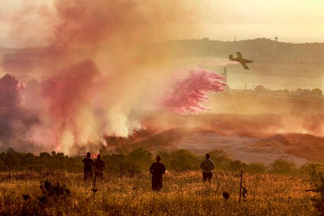Palestinians watch as an Israeli firefighting plane extinguishes a blaze near the village of Tell, adjacent to the Israeli settlement of Havat Gilad, west of Nablus in the occupied West Bank on July 18, 2026, after a reported arson attack by Israeli settlers on the village, according to eyewitnesses. (Photo by Jaafar ASHTIYEH / AFP)