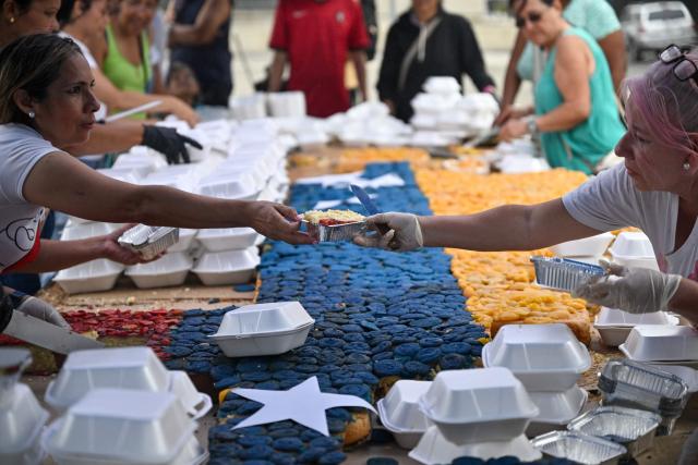 People serve portions of a giant cake in the colors of the Venezuelan national flag, to be distributed in the shelters to the people affected by the June 24 earthquakes, in Caracas on July 18, 2026. (Photo by Juan BARRETO / AFP)