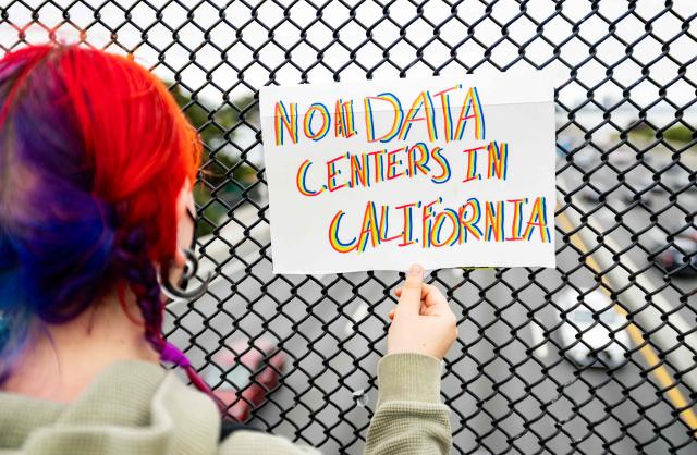 A person holds up a sign on a pedestrian bridge during a nationwide protest against AI data center expansion in Berkeley, California on July 18, 2026. (Photo by Josh Edelson / AFP)