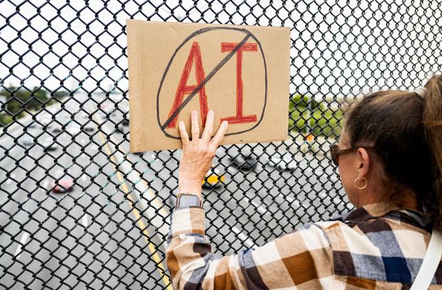 A person holds up a sign on a pedestrian bridge during a nationwide protest against AI data center expansion in Berkeley, California on July 18, 2026. (Photo by Josh Edelson / AFP)