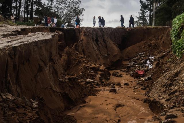 People stand next to a large sinkhole formed after heavy rains in Viсa del Mar, Chile, on July 18, 2026. Three people died and 76 were affected by a storm with heavy rains, swells, and winds that is impacting 10 of the country’s 16 regions, the government reported. (Photo by Cristobal Basaure / AFP)