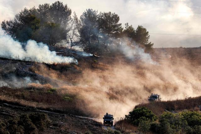 Israeli military vehicles move near fumes as a fire blazes near the village of Tell, adjacent to the Israeli settlement of Havat Gilad, west of Nablus in the occupied West Bank on July 18, 2026, after a reported arson attack by Israeli settlers on the village, according to eyewitnesses. (Photo by Jaafar ASHTIYEH / AFP)