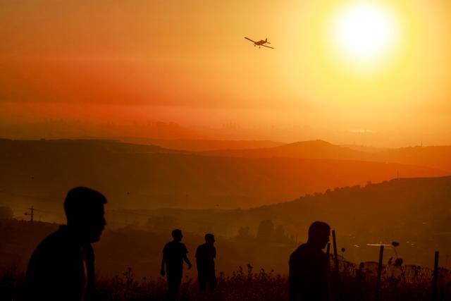 Palestinians watch as an Israeli Air Tractor AT-802 firefighting plane extinguishes a blaze near the village of Tell, adjacent to the Israeli settlement of Havat Gilad, west of Nablus in the occupied West Bank on July 18, 2026, after a reported arson attack by Israeli settlers on the village, according to eyewitnesses. (Photo by Jaafar ASHTIYEH / AFP)