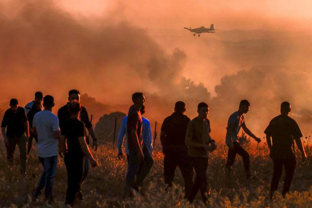 Palestinians watch as an Israeli Air Tractor AT-802 firefighting plane extinguishes a blaze near the village of Tell, adjacent to the Israeli settlement of Havat Gilad, west of Nablus in the occupied West Bank on July 18, 2026, after a reported arson attack by Israeli settlers on the village, according to eyewitnesses. (Photo by Jaafar ASHTIYEH / AFP)