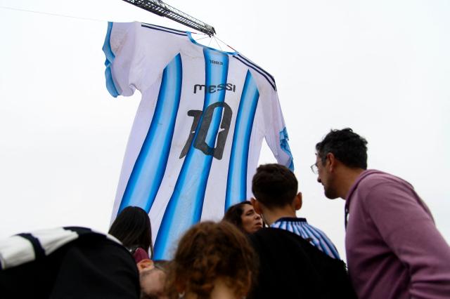 Argentina fans gather beneath a giant Argentina jersey bearing Lionel Messi's number 10 displayed near the National Flag Memorial in Rosario, Santa Fe province, Argentina, on July 18, 2026, ahead of the 2026 FIFA World Cup final between Argentina and Spain on July 19. (Photo by Marcelo Manera / AFP)