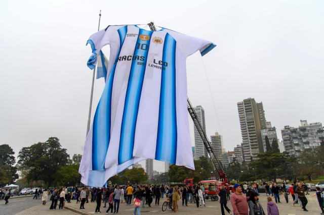 Argentina fans gather beneath a giant Argentina jersey bearing Lionel Messi's number 10 displayed near the National Flag Memorial in Rosario, Santa Fe province, Argentina, on July 18, 2026, ahead of the 2026 FIFA World Cup final between Argentina and Spain on July 19. (Photo by Marcelo Manera / AFP)