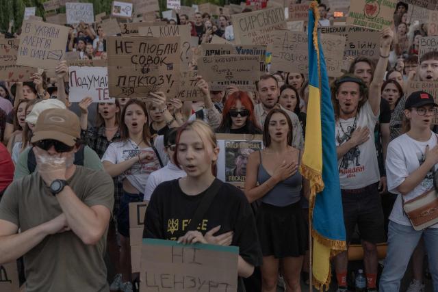 Protesters holding placards sing the Ukrainian national anthem during a demonstration against Ukraine's President's decision to dismiss Ukraine's Defence Minister Mykhailo Fedorov, and demanding the dismissal of Ukraine's army chief Oleksandr Syrskyi, in Kyiv on July 18, 2026, amid the Russian invasion of Ukraine. Large protests erupted in several Ukrainian cities against the removal of popular Defence Minister Fedorov, who had been brought in six months ago to digitise and modernise an army fatigued after four years fighting off the Russian invasion. (Photo by Roman PILIPEY / AFP)