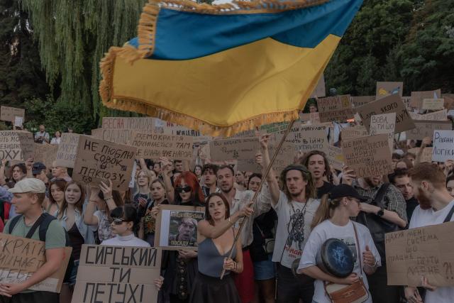 Protesters wave a Ukrainian flag, hold placards and chant slogans during a demonstration against Ukraine's President's decision to dismiss Ukraine's Defence Minister Mykhailo Fedorov, and demanding the dismissal of Ukraine's army chief Oleksandr Syrskyi, in Kyiv on July 18, 2026, amid the Russian invasion of Ukraine. Large protests erupted in several Ukrainian cities against the removal of popular Defence Minister Fedorov, who had been brought in six months ago to digitise and modernise an army fatigued after four years fighting off the Russian invasion. (Photo by Roman PILIPEY / AFP)