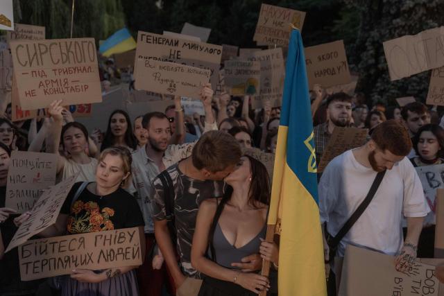 Daria and Serhii kiss each other as they attend with other protesters a demonstration against Ukraine's President's decision to dismiss Ukraine's Defence Minister Mykhailo Fedorov, and demanding the dismissal of Ukraine's army chief Oleksandr Syrskyi, in Kyiv on July 18, 2026, amid the Russian invasion of Ukraine. Large protests erupted in several Ukrainian cities against the removal of popular Defence Minister Fedorov, who had been brought in six months ago to digitise and modernise an army fatigued after four years fighting off the Russian invasion. (Photo by Roman PILIPEY / AFP)