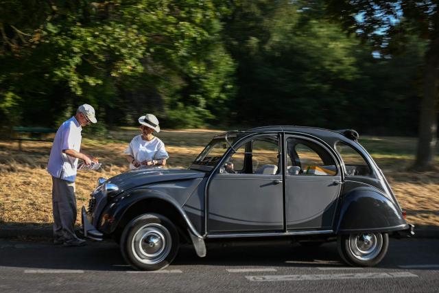 Participants stand next their Citroen 2CV during the 19th Summer parade of vintage vehicles in Paris on July 19, 2026. (Photo by Lou BENOIST / AFP)