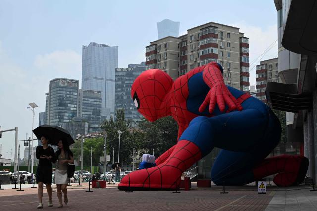 A couple walks past a giant inflatable Spider-Man outside a shopping mall in Beijing on July 19, 2026. (Photo by GREG BAKER / AFP)