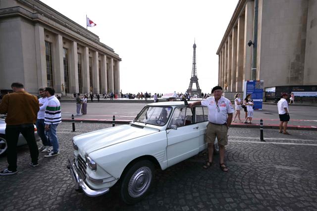 A participant poses next to his vintage Citroen Ami 6 at the Trocadero, with the Eiffel Tower seen in the background, during the 19th Summer parade of vintage vehicles in Paris on July 19, 2026. (Photo by LOU BENOIST / AFP)