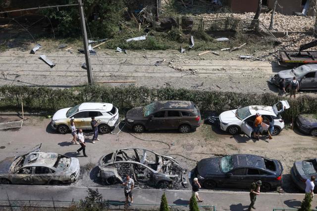 People walk past damaged cars parked in a street following missile strikes in Kyiv on July 19, 2026, amid the Russian invasion of Ukraine. Russian missiles rocked Ukraine's capital overnight, damaging residential buildings and wounding at least two people a day after Kyiv launched a wave of drone strikes deep into Russian territory. (Photo by Serhii Okunev / AFP)