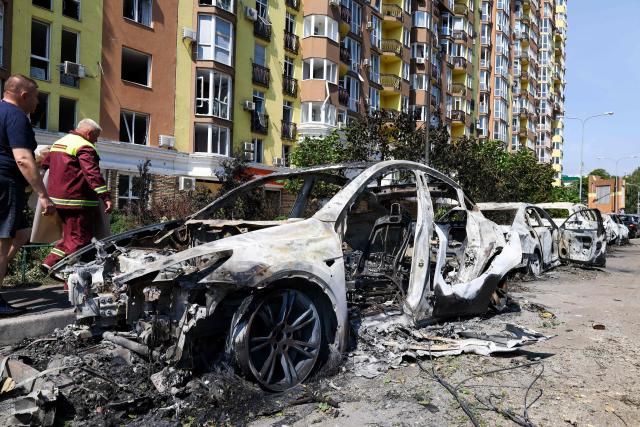 People walk past damaged cars parked in a street following missile strikes in Kyiv on July 19, 2026, amid the Russian invasion of Ukraine. Russian missiles rocked Ukraine's capital overnight, damaging residential buildings and wounding at least two people a day after Kyiv launched a wave of drone strikes deep into Russian territory. (Photo by Serhii Okunev / AFP)