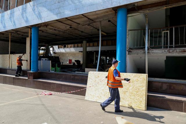 Communal workers set fiberboard to replace broken windows at the entrance to a damaged metro station following missile strikes in Kyiv on July 19, 2026, amid the Russian invasion of Ukraine. Russian missiles rocked Ukraine's capital overnight, damaging residential buildings and wounding at least two people a day after Kyiv launched a wave of drone strikes deep into Russian territory. (Photo by Serhii Okunev / AFP)