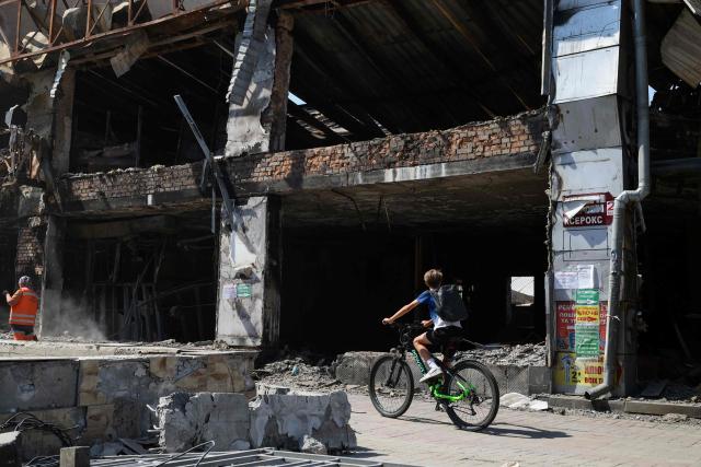 A boy rides a bicycle past a shopping mall damaged following missile strikes in Kyiv on July 19, 2026, amid the Russian invasion of Ukrain. Russian missiles rocked Ukraine's capital overnight, damaging residential buildings and wounding at least two people a day after Kyiv launched a wave of drone strikes deep into Russian territory. (Photo by Serhii Okunev / AFP)