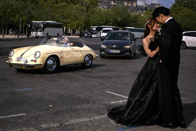 A participant drives his Porsche 356 past a couple during the 19th Summer parade of vintage vehicles in Paris on July 19, 2026. (Photo by Lou BENOIST / AFP)