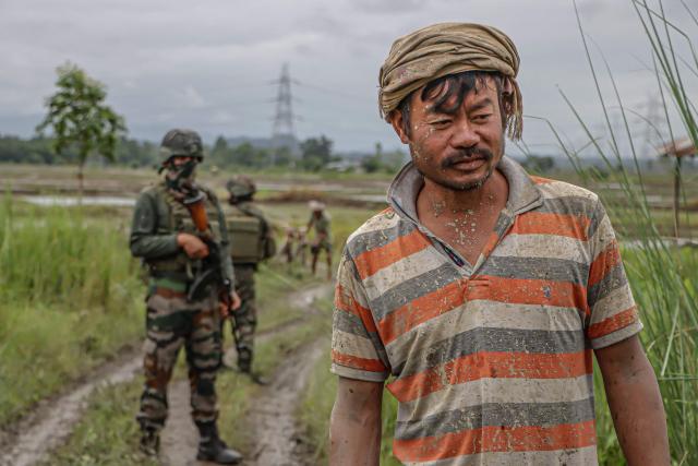 A farmer walks past security personnel at a paddy field in Imphal West, in India's northeastern state of Manipur on July 19, 2026, after cultivation disrupted by ongoing ethnic conflict resumed under tight security. (Photo by Vishma AHANTHEM / AFP)